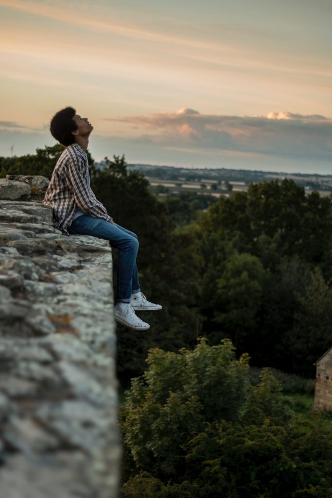 smartphone photography - A person sitting on a wall, looking skyward. Negative space in the image suggests deep thought.