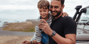 Roadtrip summer streaming tips - A man and a child looking at a phone. Smiling broadly because it's a stock photo and that's what people do in stock photos