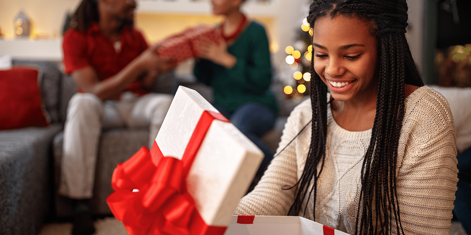 A person opens a gift and smiles. Presumably at the contents of the box but honestly, they could also be opening socks and trying to put on a happy face.